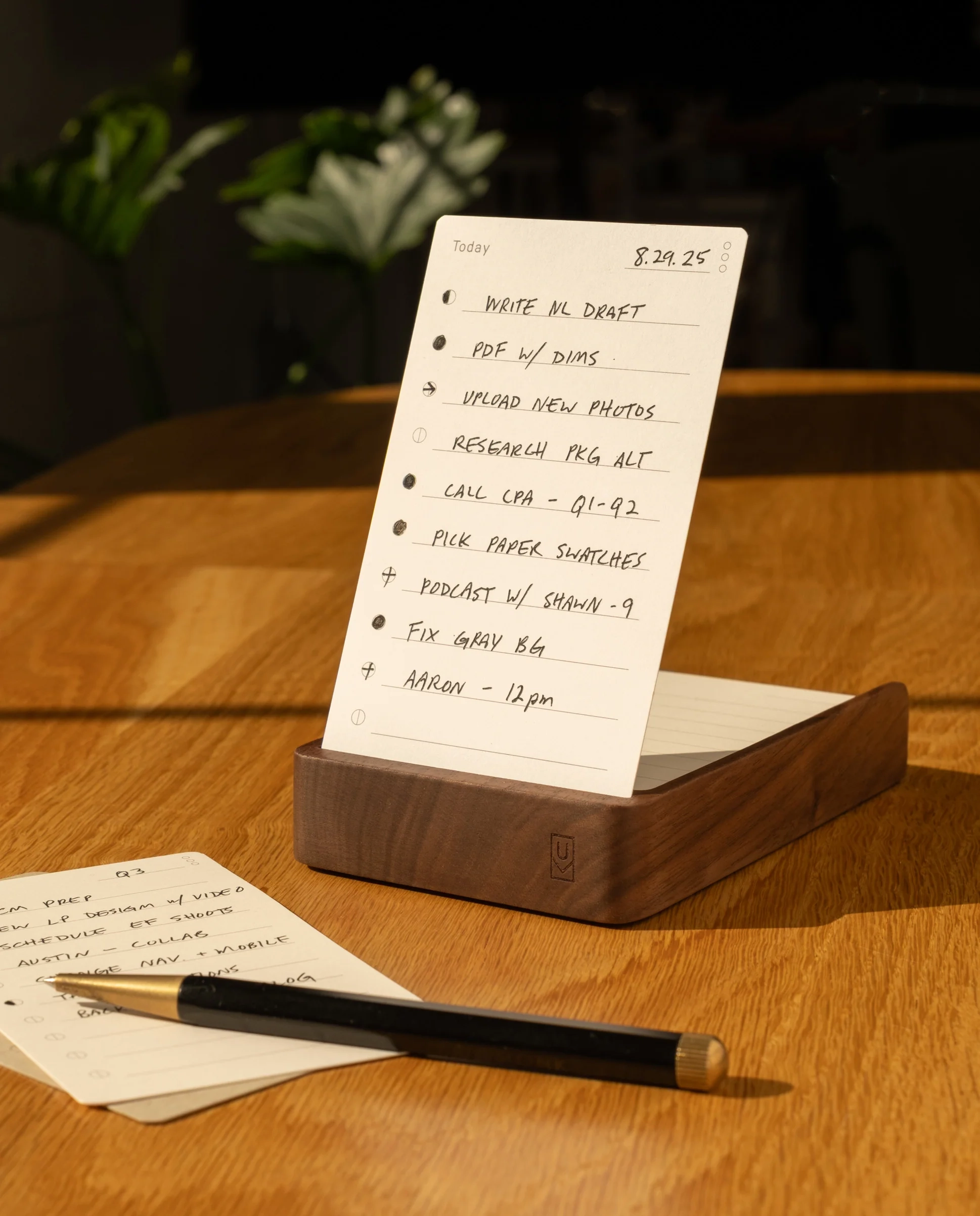The Analog Daily Focus Kit (Walnut) rests on a wooden table beside a pencil and task cards, with sunlight casting warm shadows that accentuate this simple yet effective productivity system.
